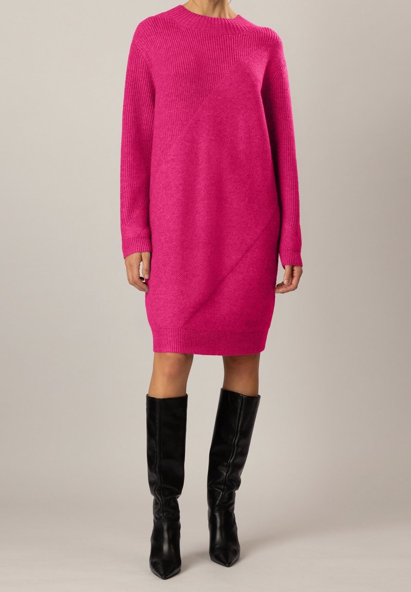 Abito rosa lavorato a maglia con scollo rotondo, maniche lunghe e un motivo a trama diagonale. Indossato con stivali neri al ginocchio.