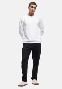 Hvid ribbet sweater med rund halsudskæring, parret med sorte bukser og hvide sneakers med brune accenter, udstyret med en afslappet pasform.