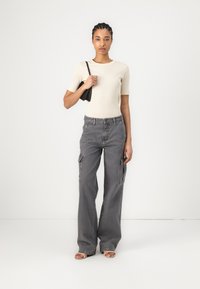 Beige ribbed short-sleeve top paired with gray wide-leg cargo pants featuring side pockets; model holding a small black handbag.