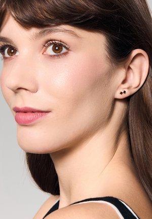 Małe geometryczne kolczyki o złoto-czarnym wzorze, w kształcie kwadratu. Modelka ma ciemne włosy i gładką cerę.