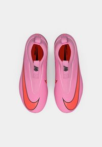 Roze atletske cipele s glatkom teksturom; imaju istaknutu crvenu Nikeovo odjelo i povlačne trake; niskoprofilni dizajn i uložak s amortizacijom.