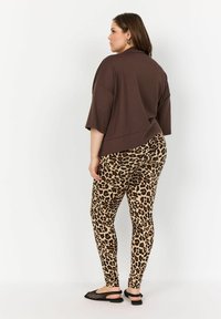 Brun oversized topp som bärs tillsammans med leggings med leopardmönster. Toppens passform är lös och har korta ärmar, medan leggingsen har en mjuk textur.
