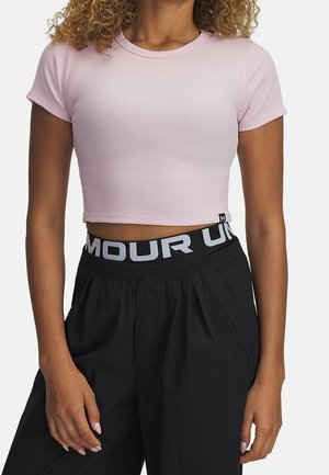 Kvinde iført en lyserød kortærmet croppet top og sorte bukser med en synlig Under Armour linning.