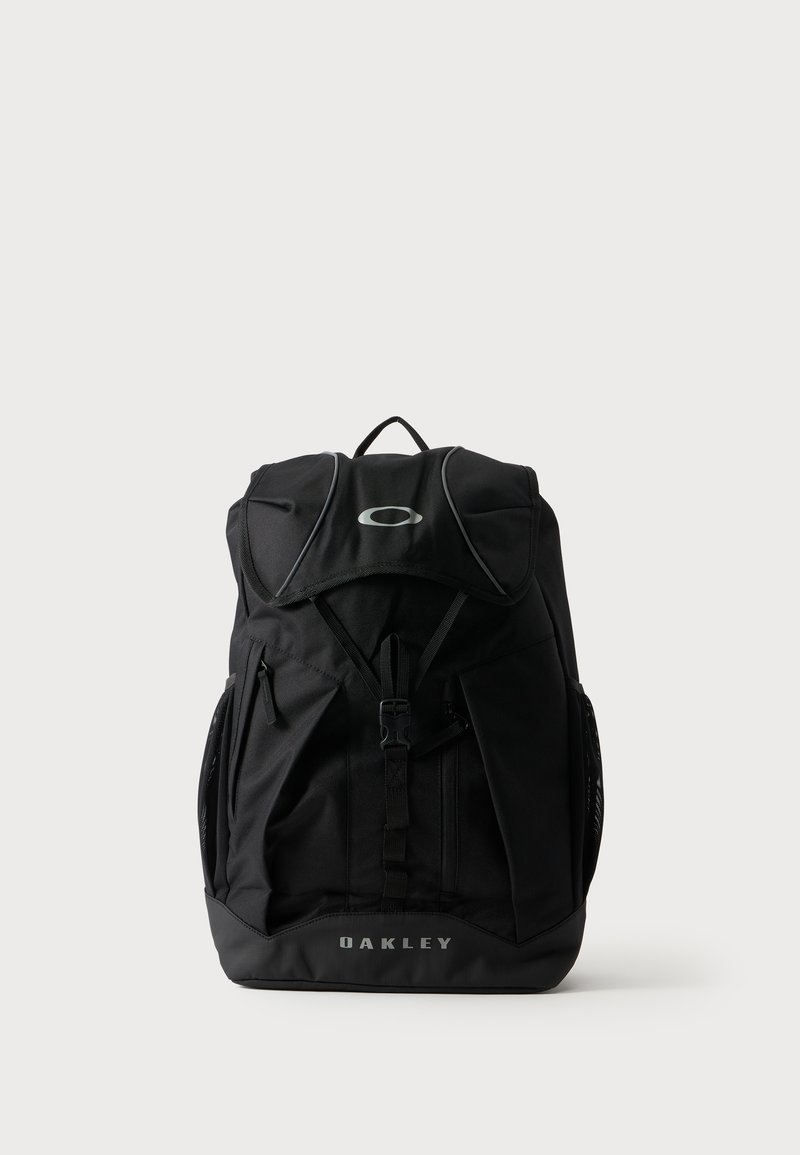 Μαύρο σακίδιο Oakley με εμπρόσθιο κουμπί, πολλαπλές θήκες με φερμουάρ και επάνω χειρολαβή σε απλό ανοιχτό φόντο.