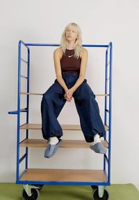 Un'unità di scaffalatura in metallo blu con ripiani in legno, che presenta una persona seduta con pantaloni in denim scuro larghi e scarpe grigio chiaro.
