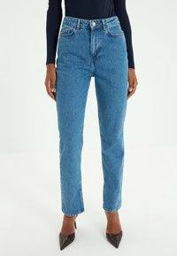 Jean en denim bleu clair taille haute avec une coupe droite, comprenant deux poches avant et une fermeture à bouton à l'avant.