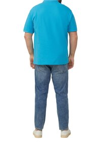 Polo turquoise à manches courtes, associé à un jean bleu clair et des baskets blanches, vu de dos. Design et coupe décontractés.