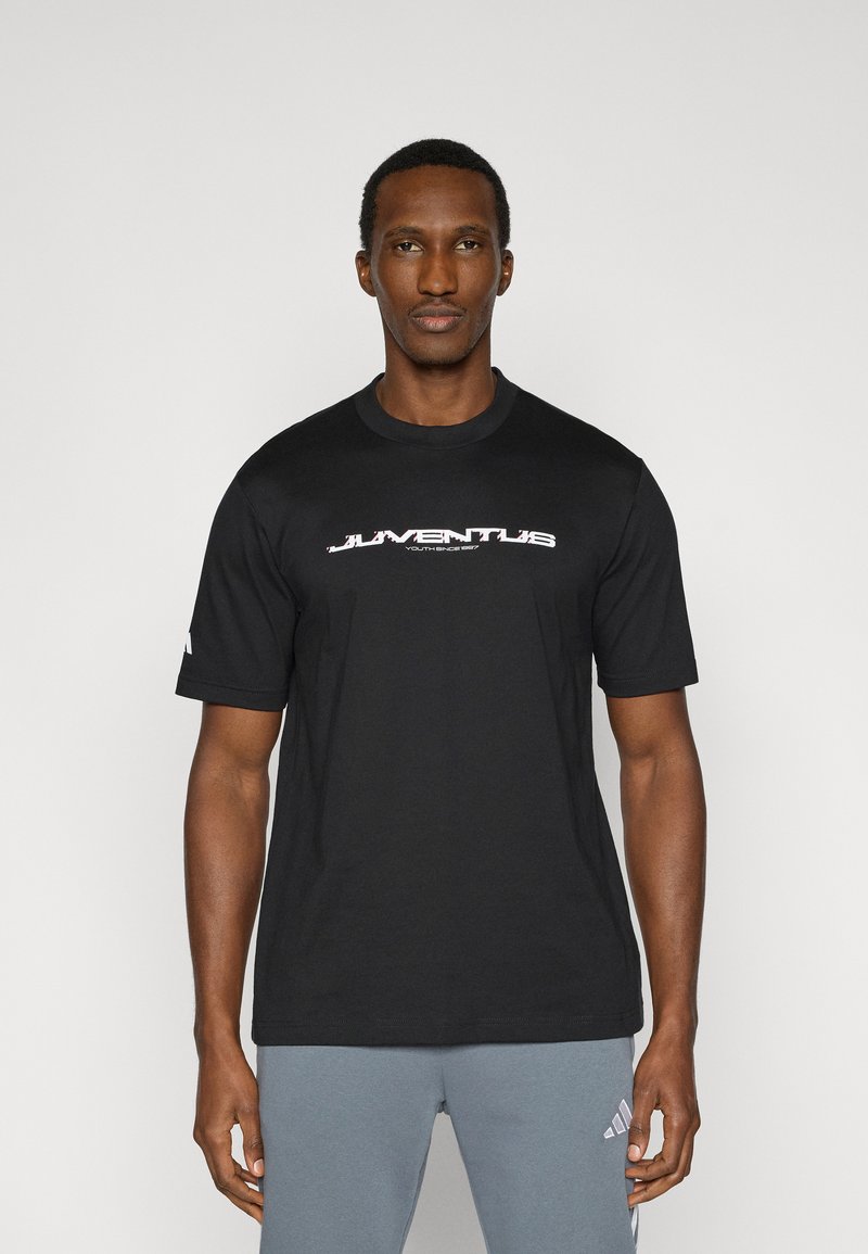 Μαύρο βαμβακερό t-shirt με το λογότυπο "JUVENTUS" σε λευκό και κόκκινο, κοντά μανίκια, στρογγυλή λαιμόκοψη, φορεμένο με γκρι αθλητικό παντελόνι.