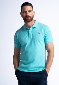 Tyrkysové polo tričko vyrobené z bavlny, s límečkem a krátkými rukávy. Má malé černé logo na levé části hrudi.
