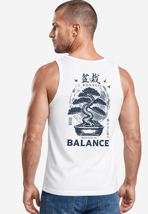 Mann trägt weißes Tanktop mit Bonsai-Baum-Grafik und dem Text "Bonsai Rooted in Balance" auf dem Rücken vor weißem Hintergrund.