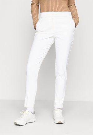 Bílé kalhoty na míru s hladkým povrchem, slim fit, bočními kapsami a knoflíkovým zapínáním v pase. Oblékané s botami na světlé barvě.