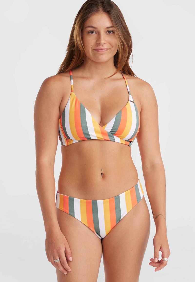 Jeune femme portant un bikini rayé vertical multicolore avec des fines bretelles, se tenant devant un fond blanc uni, faisant face à l'avant.