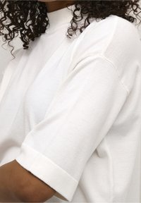 Top corto bianco in cotone a maniche corte con collo alto e risvolti, caratterizzato da una texture liscia e una vestibilità rilassata.