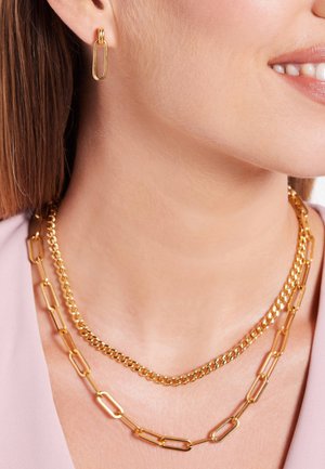 Gouden juwelenset bestaande uit een verbonden kettinghalsketting en bijpassende ovale hangertjes, met een gepolijste afwerking en een gladde textuur.