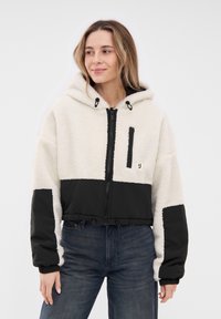 Fleece-lined cropped jacket with a white, plush body and black nylon sleeves. Features a front zipper, hood, and a zipped chest pocket.