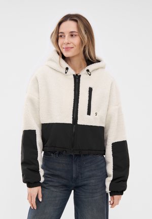 Fleece-gevoerd cropped jack met een witte, pluche body en zwarte nylon mouwen. Voorzien van een ritssluiting aan de voorkant, een capuchon en een ritsborstzak.