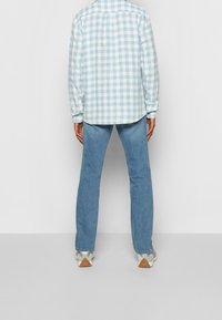 Blå och vit rutig långärmad skjorta med knappmanschetter, tillsammans med ljusblå jeans och vita sneakers med texturerad sula.