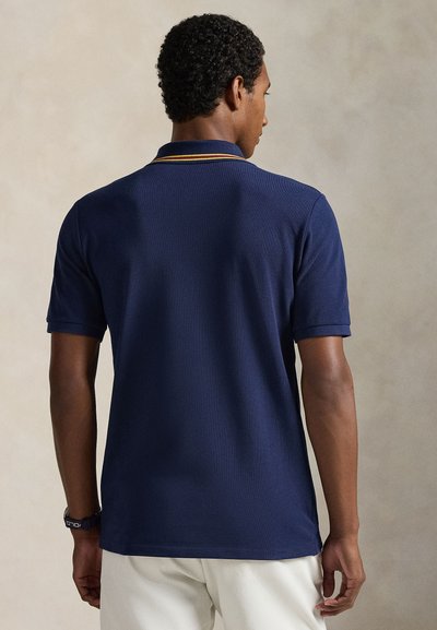 Μπλούζα πόλο σε ναυτικό μπλε χρώμα με ριμπ υφή, κοντά μανίκια και κολάρο σε αντίθετο κίτρινο χρώμα. Απλός και εφαρμοστός σχεδιασμός.