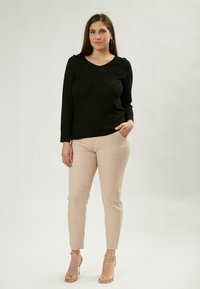 Schwarzes Langarmshirt mit V-Ausschnitt und strukturiertem Chevron-Muster, kombiniert mit enganliegenden beigen Hosen und goldenen Riemchensandalen. Einfache Hintergründe.