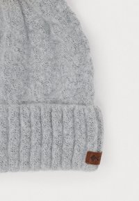 Pelēks adīts beanie, kas izceļas ar kabelveida rakstu un ribotu malu. Iekļauts neliels brūns ādas birka ar logotipa detaļu. Mīksta, teksturēta auduma.