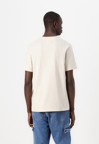 Beige cotton t-shirt with short sleeves and a V-shaped back neckline, paired with blue denim cargo shorts featuring patch pockets.