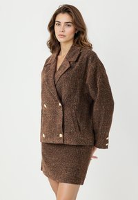 Braune strukturierte Jacke mit passendem Rock. Doppelreiher-Design mit goldenen Knöpfen und Reverskragen. Weiches Strickmaterial.