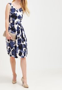 Vestido floral con un cuerpo ajustado y falda amplia, en colores azul marino y blanco. Tejido suave con grandes patrones de flores y cremallera oculta.