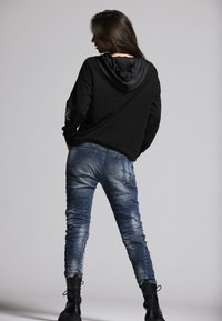 Black hoodie with a textured finish and a drawstring hood, paired with faded blue jeans featuring a slim fit and distressed accents. Black boots.