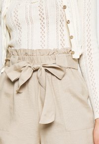 Béžové šortky s vysokým pasem, se staženým pasem a detailem na zavázání. Vyrobené z lehkého materiálu, s dvěma předními kapsami.