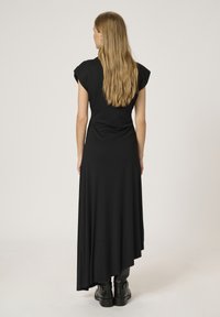 Abito maxi nero con maniche corte, orlo asimmetrico, realizzato in tessuto morbido. Abbinato a stivali neri alla caviglia. Texture liscia, design minimal.