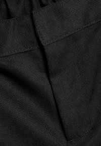 Tissu noir avec un tissage texturé, présentant une finition lisse et des coutures visibles ; deux poches aux bords droits sont présentes.