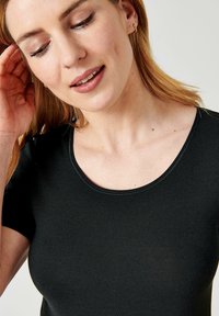 Maglietta nera a coste con scollatura a girocollo e maniche corte, realizzata in tessuto morbido; presenta una leggerissima lucentezza e una consistenza elasticizzata.