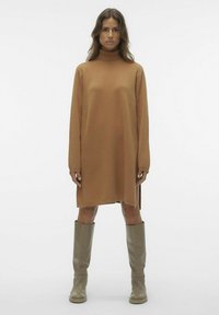 Pulover obleka s turtleneck ovratnikom v svetlo rjavi barvi, z dolgimi rokavi in stranskimi razporki, v kombinaciji z bež škornji do kolen. Gladka tekstura.
