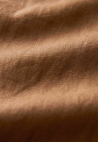 Textile brun avec une surface douce et texturée. Le tissu semble légèrement froissé, mettant en valeur un aspect naturel et organique.