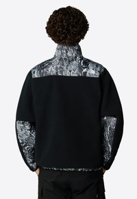 Czarny polarowy pulower z wysokim kołnierzem, z wzorzystą tekstylną wstawką na ramionach i rękawach w odcieniach białego i szarego.