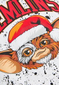 Bomulds T-shirt med en tegneseriefigur med orange-brun pels og store øjne, iført en rød julekasket, på en hvid spraglet baggrund.