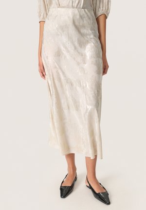 Silky, cream-colored midi skirt with a subtle abstract pattern and a relaxed fit. Paired with black, pointed-toe slingback shoes.