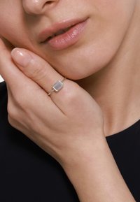 Anello d'oro con una pietra rettangolare di un leggero colore viola, montata su una delicata fascia con piccoli accenti rotondi attorno alla pietra.