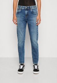 Light blue denim jeans with a straight fit, five pockets, and a button closure. Worn with black and white sneakers.