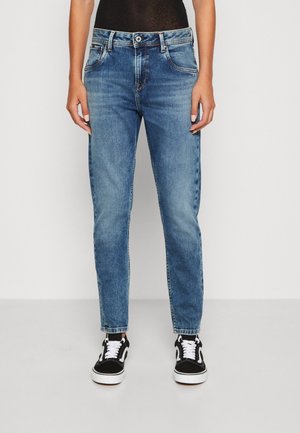 Jean en denim bleu clair avec une coupe droite, cinq poches et une fermeture à bouton. Portés avec des baskets noires et blanches.