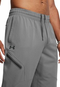 Graue Jogginghosen mit elastischem Bund, verstellbarem Kordelzug, seitlichem Reißverschluss-Stubenfach und dezentem Logodesign. Glattes, strukturiertes Material.