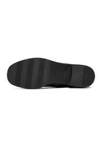 Suela de zapato negra con superficie lisa y ranuras horizontales y verticales alternadas para tracción, punta redondeada y branding sutil.