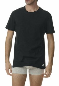 Czarna bawełniana koszulka z krótkimi rękawami i okrągłym dekoltem. Posiada małe białe logo Adidas na dolnej lewej stronie.