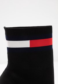 Černá ponožka s ribbed texturou, která má na vrchu horizontální pruh červených, bílých a modrých pruhů.