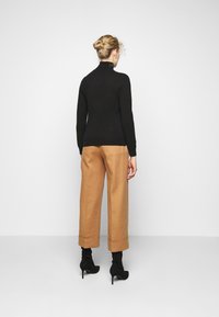 Svart turtleneck genser, tettsittende, parret med beige vide bukser. Modellen har på seg svarte hæl ankle boots. Bakfra mot en nøytral bakgrunn.