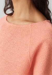 Maglione a maniche corte, in un morbido rosa corallo con scollo ampio. Il tessuto appare soffice e leggermente peloso, con una vestibilità rilassata.