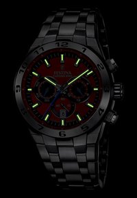 Montre en acier inoxydable noir avec un cadran rouge, des index horaires lumineux verts, des sous-cadrans chronographe et un affichage de la date à la position de 6 heures.