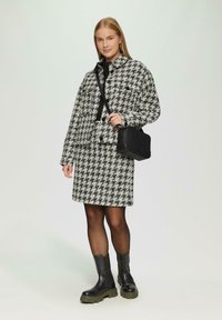 Hahnentritt-Muster Jacke und Rock in Schwarz und Weiß, kombiniert mit schwarzen knielangen Stiefeln und einer strukturierten schwarzen Handtasche.
