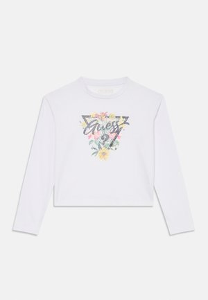 Crop top blanc à manches longues avec un design graphique coloré de motifs floraux et le mot "Guess" en police noire scintillante.