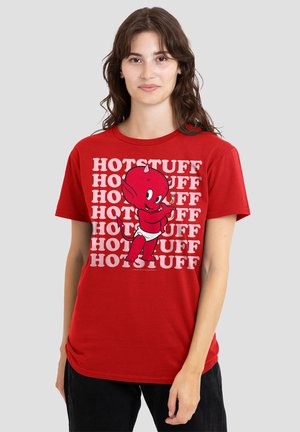 Young person wearing a red T-shirt with repeated "HOT STUFF" text and a cartoon red devil baby holding a small flame.